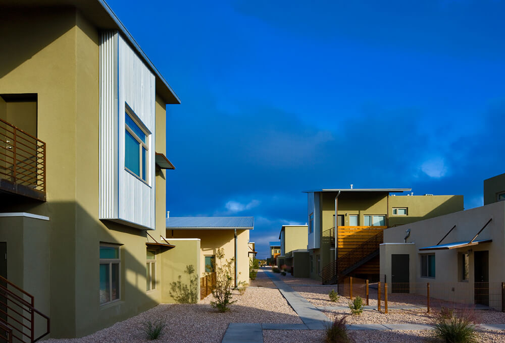 Gravel courtyard walkway between two-story apartment homes under a deep blue sky at La Pradera, Hobbs NM