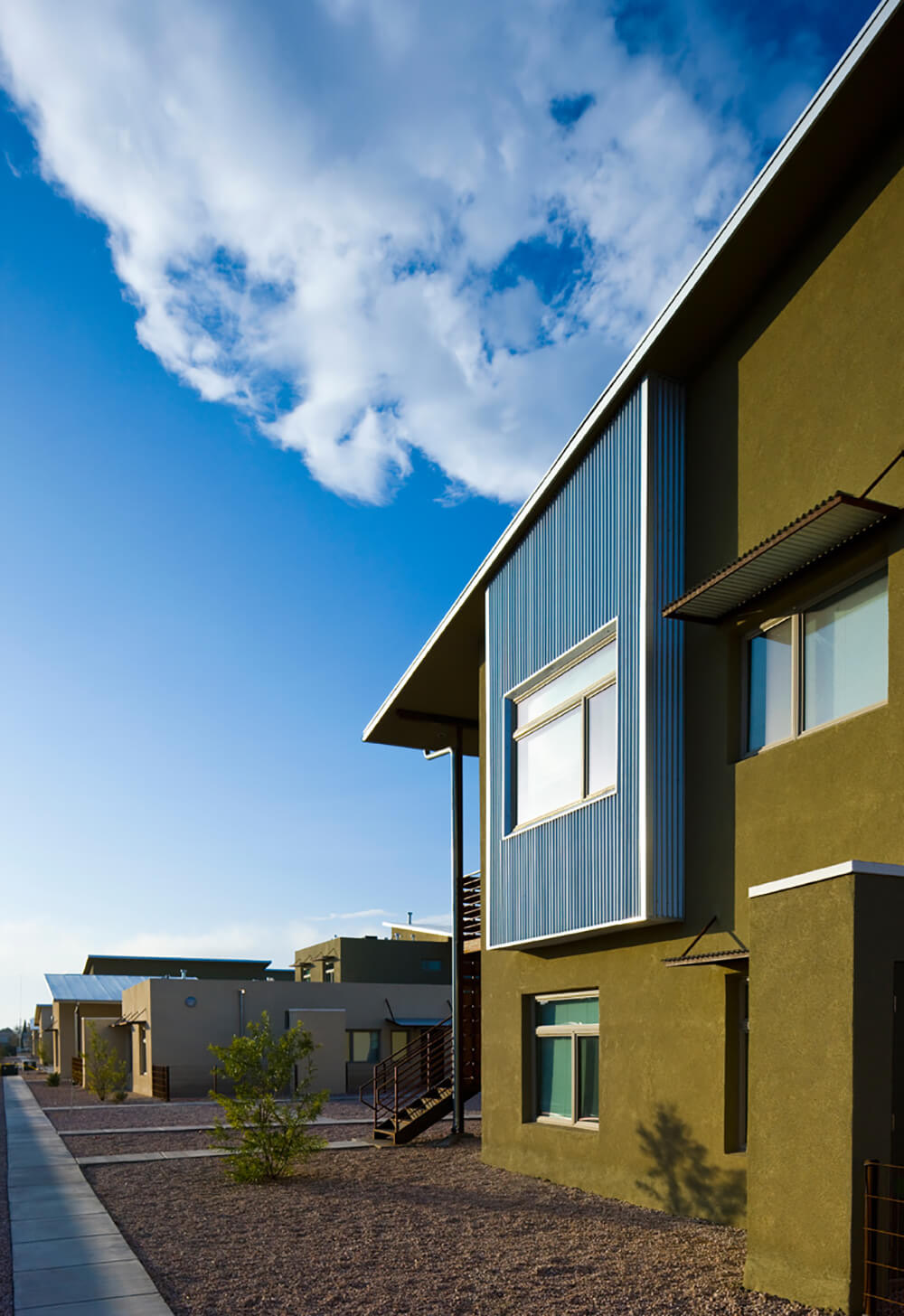 Sidewalk past apartment homes with clerestory windows and desert landscaping at La Pradera