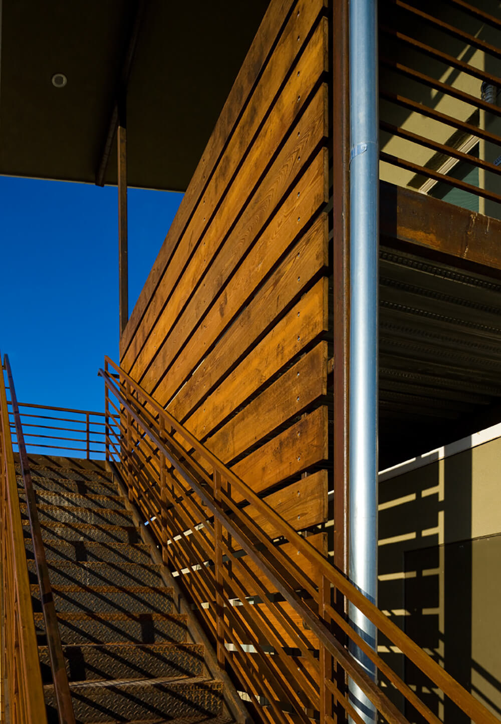 Wood privacy screen and steel exterior stairway detail in afternoon light at La Pradera