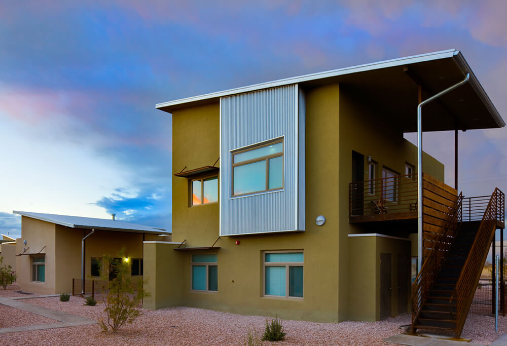 Two-story apartment home with a steel stairway and balcony under a sunset sky at La Pradera in Hobbs