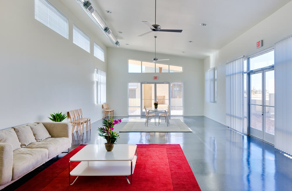 Bright community building interior at La Pradera with lounge seating, a dining table, and polished concrete floors